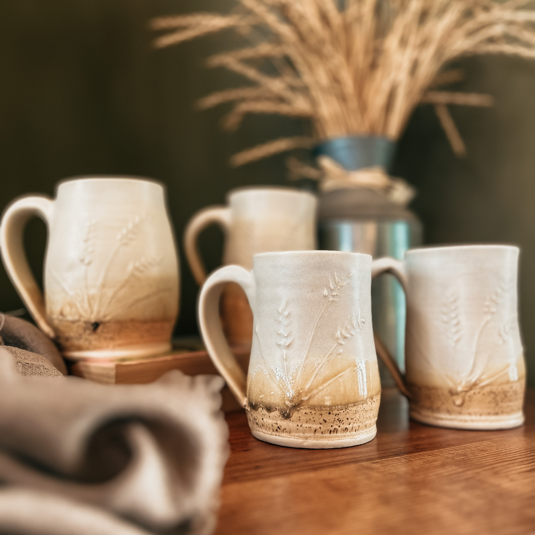 Four harvest mugs sitting on a brown table with a grain decoration in the background