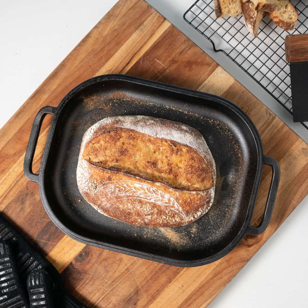 A loaf of bread in a Challenger Breadpan cast iron pan on a cutting board, made with whole grains from Canada. 